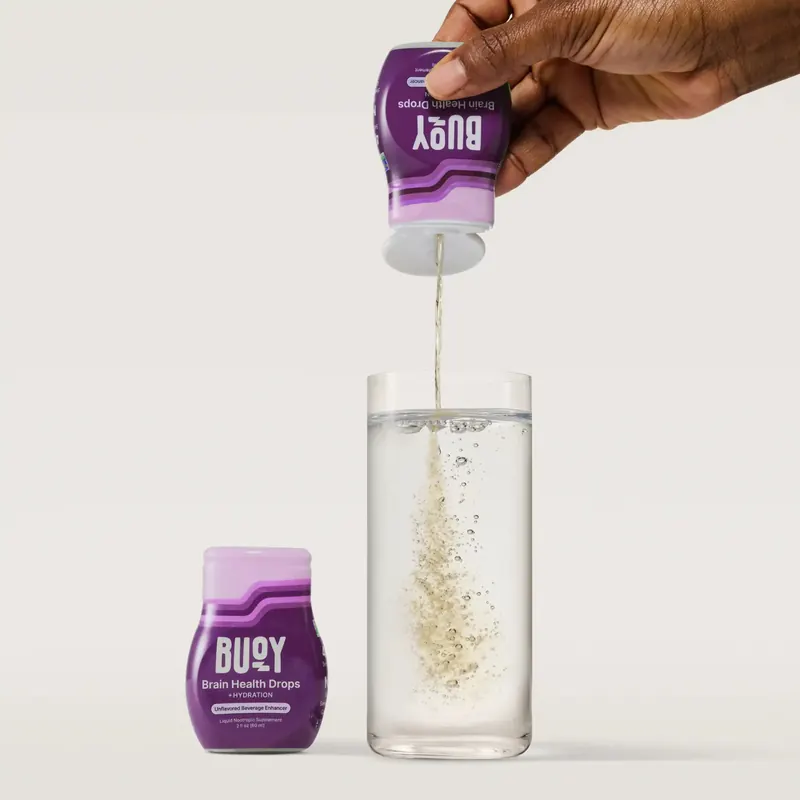 A single purple squeeze bottle beside a tall glass of water into which a squeeze of clear liquid is falling